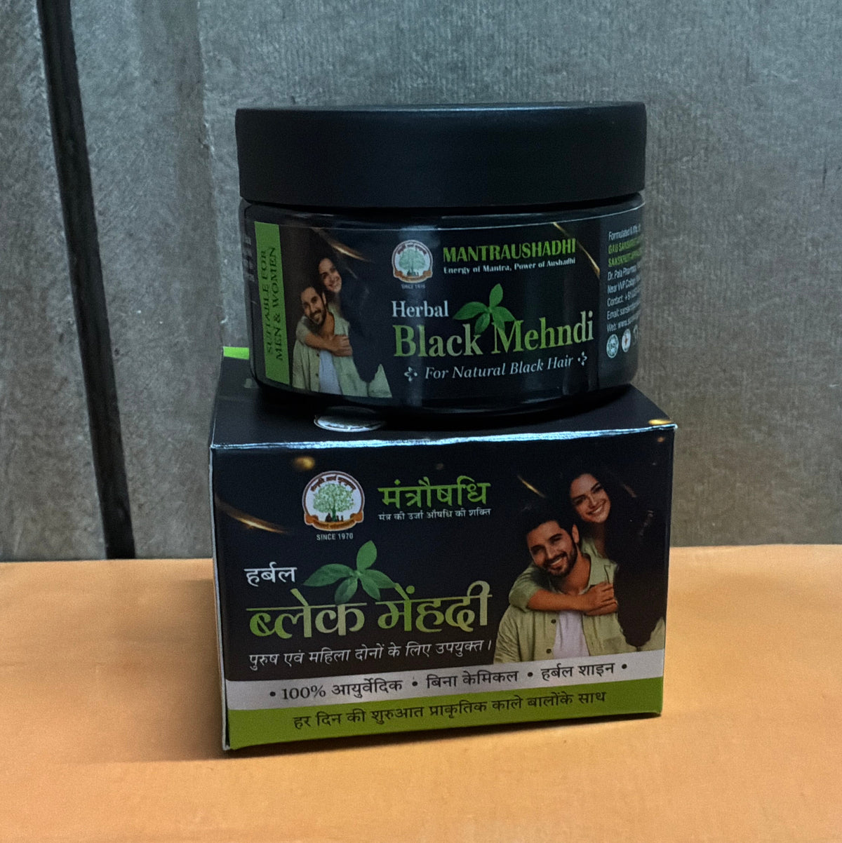 A jar of Masterkarmoo Herbal Black Mehndi placed on top of its retail box, set on a brown cardboard box against a gray wall.